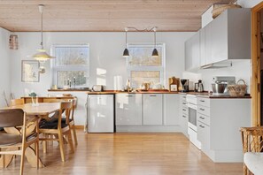 A modern kitchen with white cabinets, wooden countertops, and a dining area with a wooden table and chairs. - Cozy wooden cottage close to nature and beach (Vig)