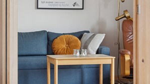 Un sofá azul con una mesa de vidrio, un sillón de cuero marrón y una obra enmarcada en la pared.