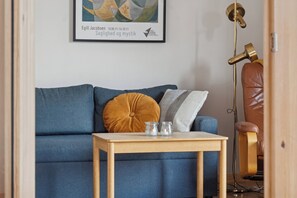 Un sofá azul con una mesa de vidrio, un sillón de cuero marrón y una obra enmarcada en la pared.