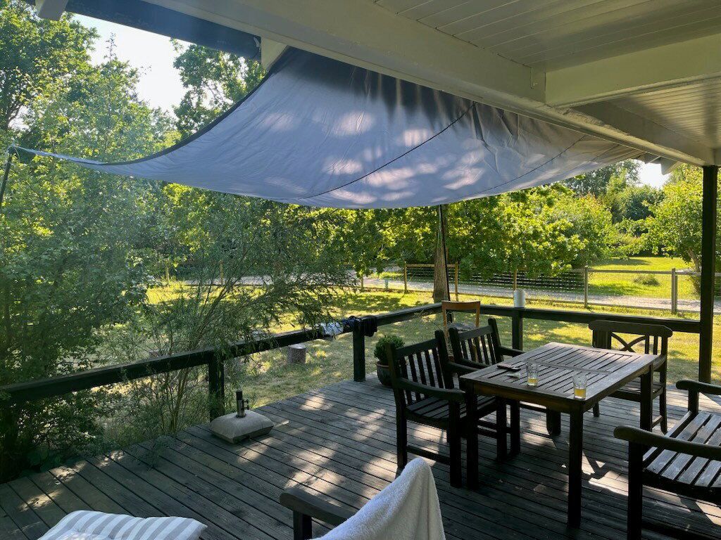 A wooden deck with outdoor furniture, a covered area with a canopy, and a view of a green landscape.