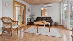 Una habitación con techo de madera, una silla de mimbre, un sofá de cuero negro, una mesa redonda y un amplio ventanal.