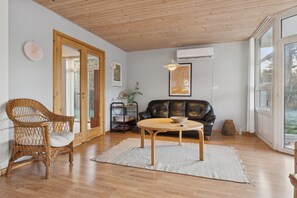 Una habitación con techo de madera, una silla de mimbre, un sofá de cuero negro, una mesa redonda y un amplio ventanal.