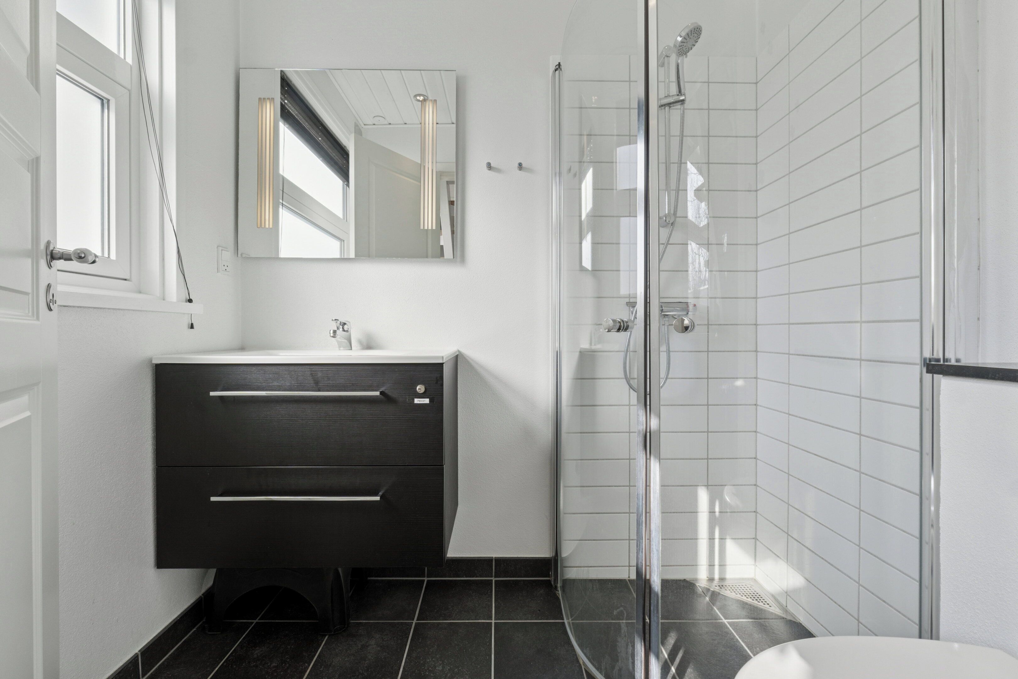 Une salle de bain moderne avec un meuble-lavabo foncé, une douche en verre et des murs recouverts de carreaux blancs.