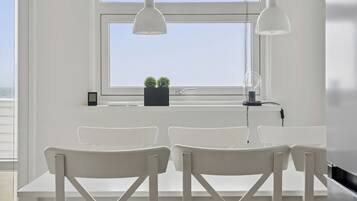 Une pièce dotée d’une grande fenêtre, de chaises blanches, d’une petite table et de luminaires suspendus.