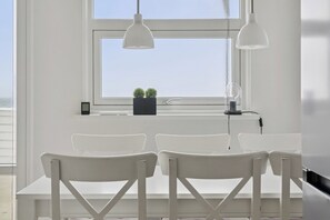 A room with a large window, white chairs, a small table, and pendant lights. - Seafront holiday home 4 ppl 30 m sea (Otterup)