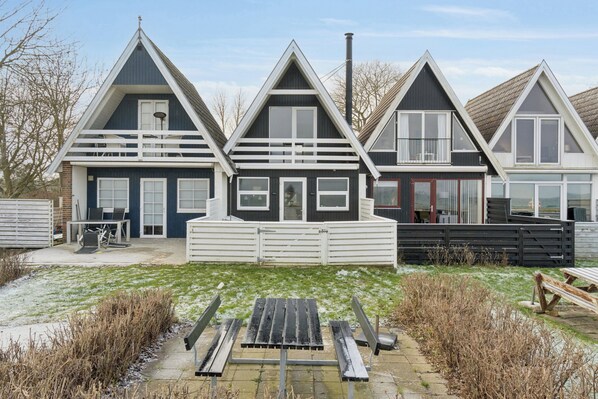 Une rangée de trois maisons avec des toits à pignon, une terrasse en bois et un banc en métal au premier plan.