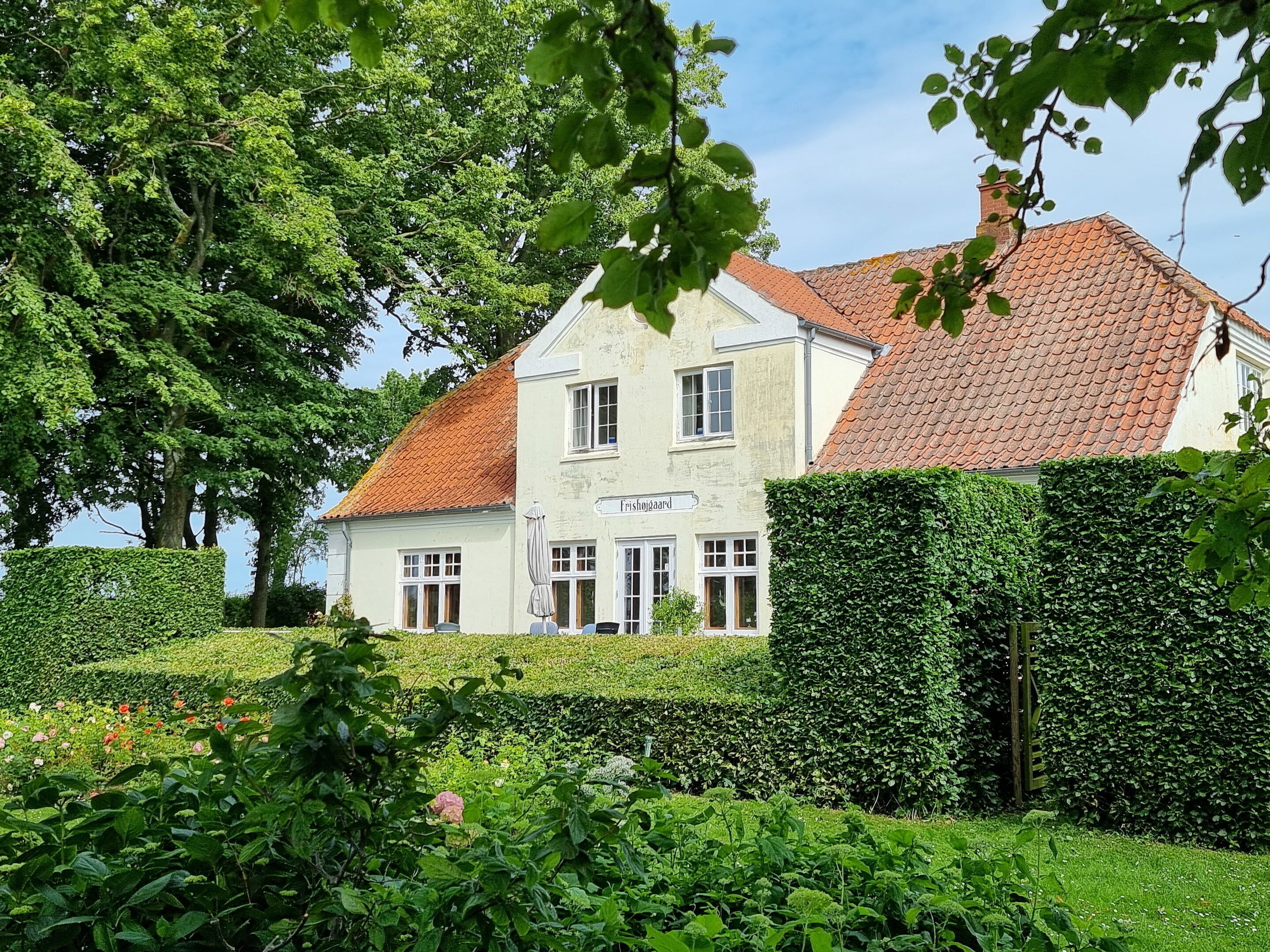 A two-story building with a tiled roof, surrounded by lush greenery and a well-maintained hedge.
