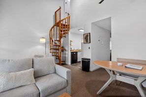 A modern living room with a sofa, a wooden staircase, a kitchen area, and a dining table.