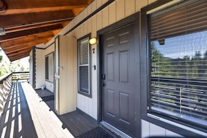 A wooden deck with a covered area, a dark-colored door with a number, and a window with blinds.
