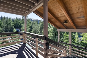 A wooden deck with a railing, a ceiling fan, and a view of a forested area.