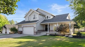 A two-story house with a garage, a covered porch, and a well-maintained lawn. - Grand Mountain Retreat: Hot Tub, Sleeps 21, Sofa Sleeper on Main Floor (Draper)