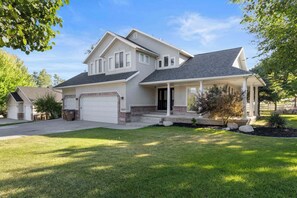 A two-story house with a garage, a covered porch, and a well-maintained lawn. - Grand Mountain Retreat: Hot Tub, Sleeps 21, Sofa Sleeper on Main Floor (Draper)