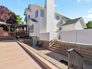 Une maison à deux étages avec un escalier en pierre, un patio couvert et une cour clôturée.