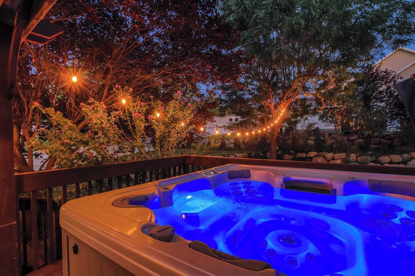 Una vasca idromassaggio illuminata da una luce blu, circondata da alberi e luci decorative.