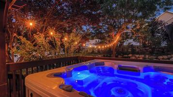 Una vasca idromassaggio illuminata da una luce blu, circondata da alberi e luci decorative.