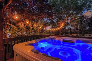 Un bain à remous avec un éclairage bleu, entouré d’arbres et illuminé de guirlandes lumineuses.