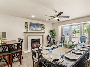 A dining room with a fireplace, a ceiling fan, and a large window offering a view of the outdoors. - Grand Mountain Retreat: Hot Tub, Sauna, Sleeps 21, Sofa Sleeper on Main Floor (Draper)