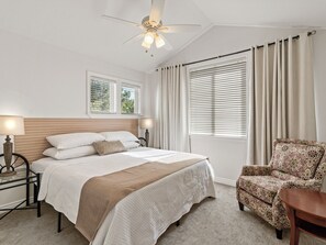 Une chambre à coucher comprenant un lit, des lampes de chevet, un ventilateur de plafond, une fenêtre avec des stores, une chaise et une table.