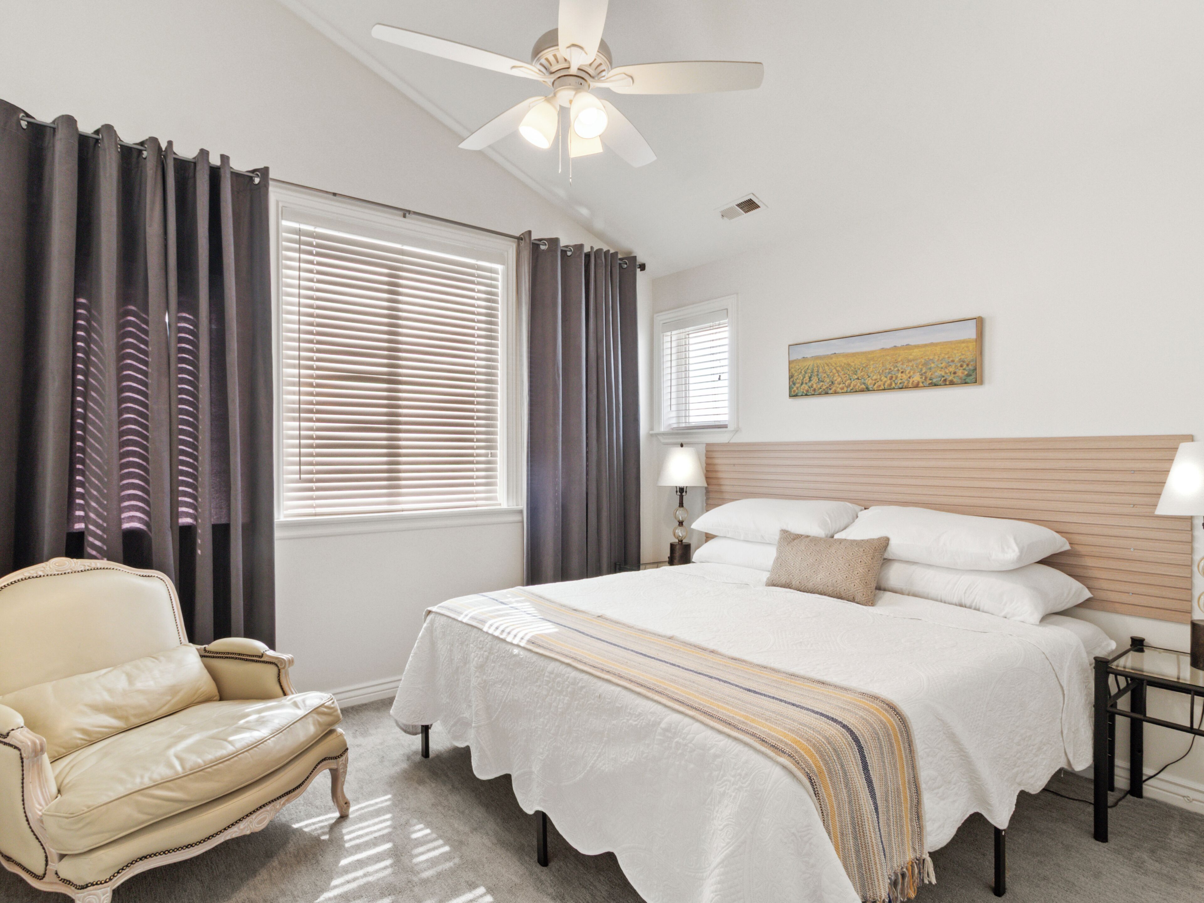 A bedroom with a bed, a chair, a ceiling fan, and a window with curtains.