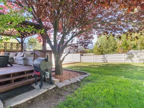A backyard with a grill, outdoor furniture, a tree, and a wooden deck. - Grand Mountain Retreat: Hot Tub, Sleeps 21, Sofa Sleeper on Main Floor (Draper)