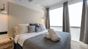 Une chambre d’hôtel moderne avec un grand lit, une table de chevet, une lampe et une fenêtre avec des rideaux.