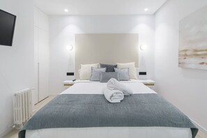 A modern hotel room with a large bed, bedside tables, a flat-screen TV, and a painting on the wall. - Deluxe SOL, by MONARo 2BR 1BTH Exterior. (Madrid)