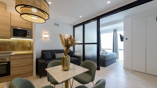 Un espace de vie moderne comprenant une cuisine, un coin repas et une grande porte coulissante donnant accès à une chambre.