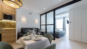 Une chambre d’hôtel moderne comprenant un coin repas aménagé pour quatre personnes, un canapé, un lit et une porte-fenêtre coulissante donnant sur un balcon.