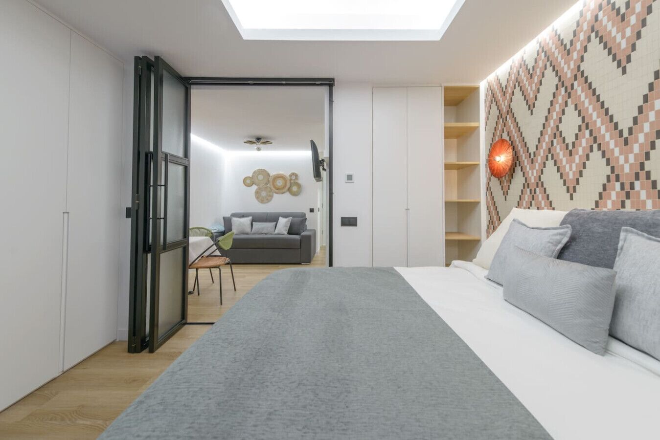 Quarto moderno com claraboia, cama com roupa de cama cinza, tapete cinza e parede estampada.