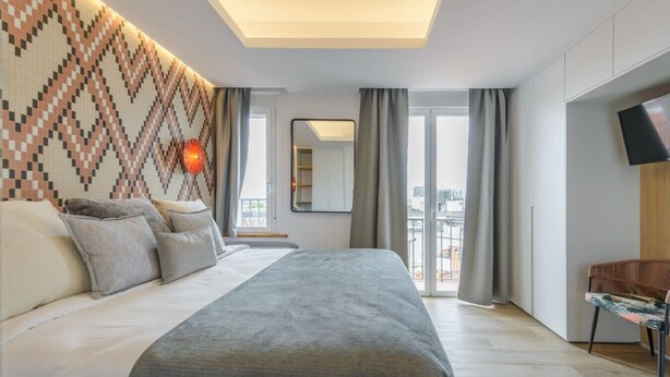 Une chambre moderne avec un grand lit, un mur décoré de motifs, une télévision et un balcon agrémenté de rideaux.