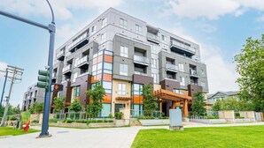 A multi-story residential building with balconies, a covered outdoor area, and a well-maintained lawn. - Downtown Condo near Vancouver Skytrain (Surrey)