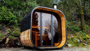Een moderne, cilindervormige houten hut met grote glasramen, gelegen in een bebost gebied.
