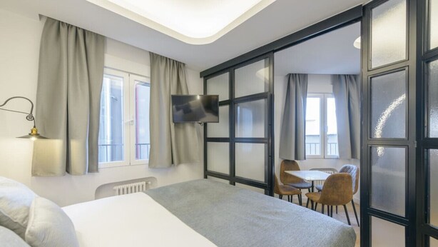 Hotellihuone, jossa on sänky, työpöytä, tuoli, televisio ja ikkuna, jossa on verhot.