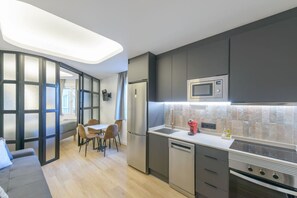 A modern kitchen with a built-in microwave, oven, and dishwasher. There is a dining area with a table and chairs. - GRAN VIA capitals, NEW YORK (Madrid)