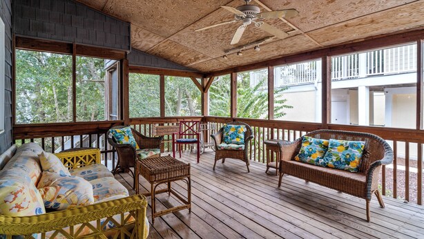A covered porch with wicker furniture, a ceiling fan, and large windows overlooking a wooded area. - 5 Bdrm Beach House-Walk to Beach-Pet Friendly (North Myrtle Beach)