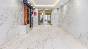 Un hall d’hôtel doté d’un sol et de murs en marbre, d’une entrée avec une porte en verre et d’un mur décoratif en bois.