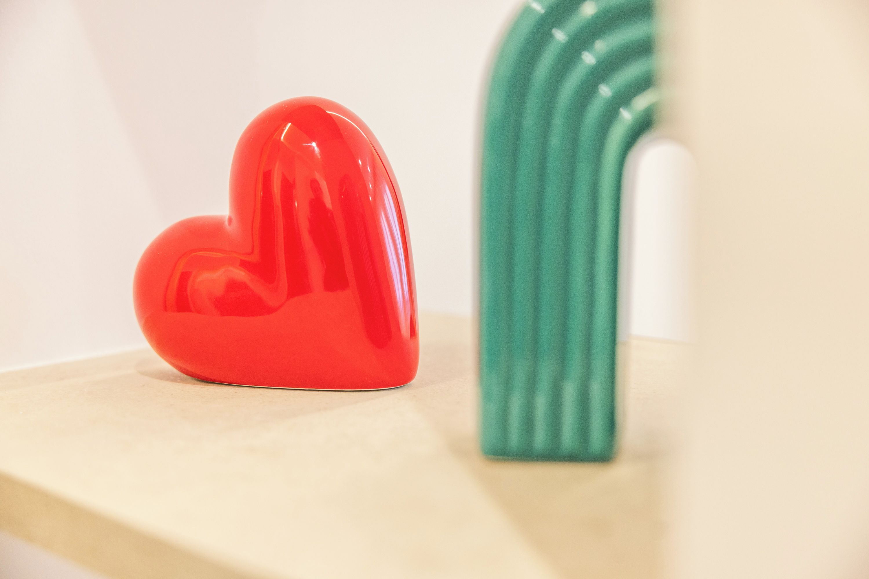 A red heart-shaped object and a green vertical object on a light-colored surface.