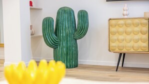 Un cactus, un bol décoratif jaune et une chaise de style vintage dans une pièce au plancher en bois et aux murs blancs.