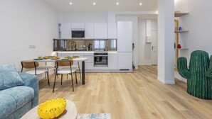 Une cuisine moderne avec des meubles blancs, un coin repas doté d’un canapé bleu et une plante, un cactus.