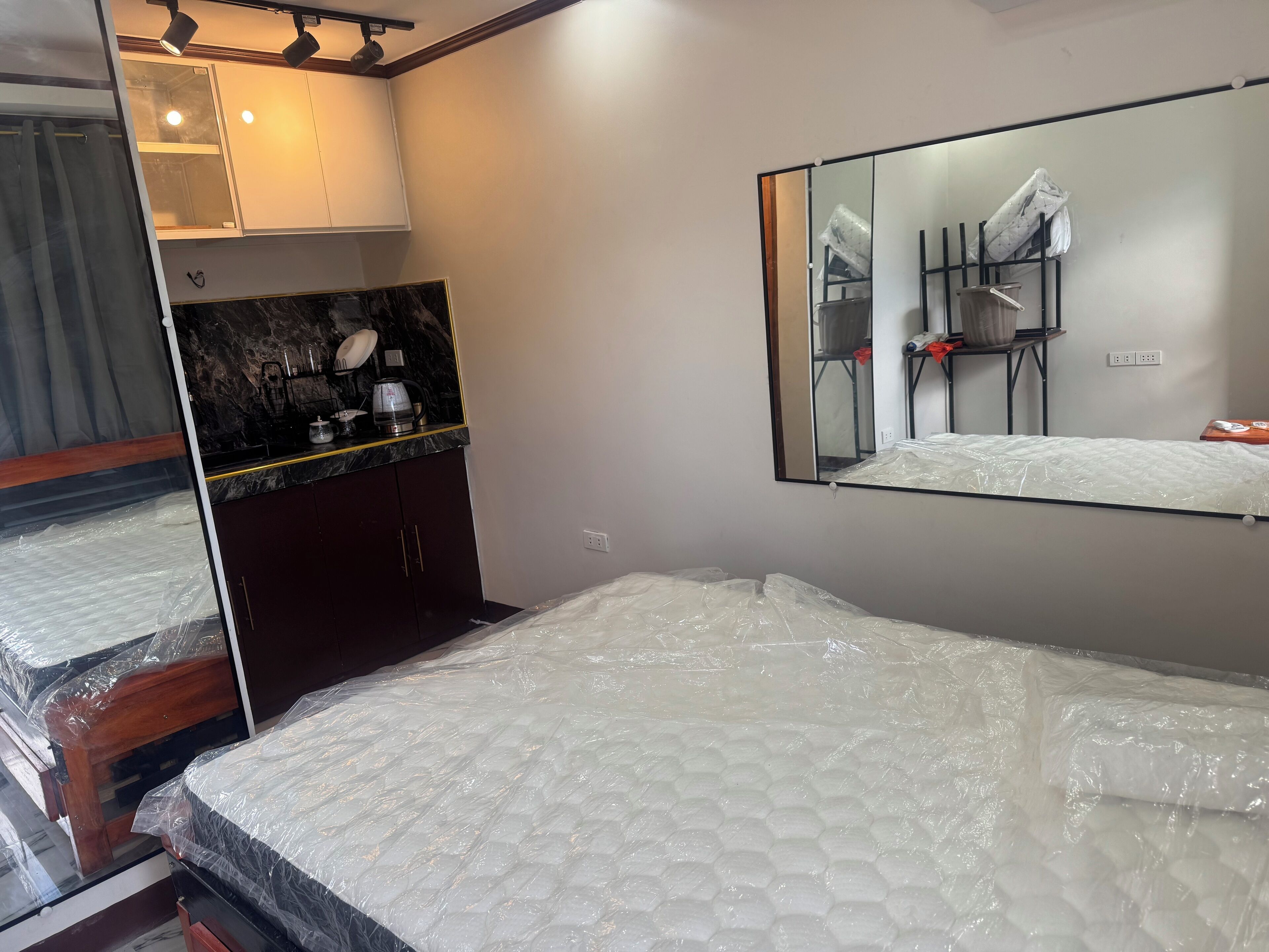 Une chambre d’hôtel avec un lit, une petite kitchenette, un miroir et une fenêtre.
