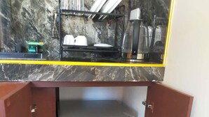 Eine Küchenzeile mit Marmorfliesenspiegel, einem Kühlschrank mit Werbeaufkleber und einem Regal mit Geschirr und Gläsern.