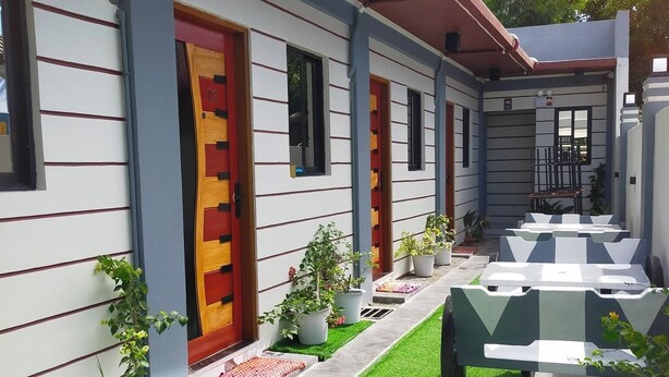 Ein Gebäude mit roter Tür, zahlreichen Fenstern und Außenbereich mit Kunstgrasanlage.