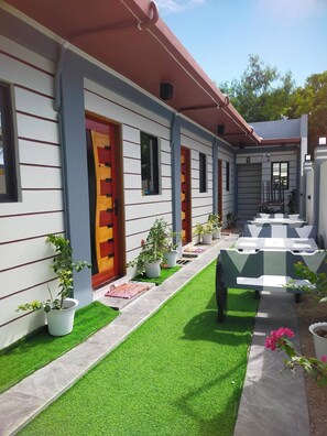 A building with a red door, multiple windows, and outdoor seating with artificial grass. - Kabayan Hotel (Aliaga)