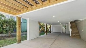 Un amplio espacio techado al aire libre con piso de concreto, vigas de madera y una escalera que lleva a un garaje.