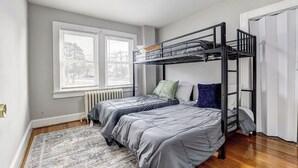 Ein kleines Schlafzimmer mit zwei Einzelbetten, einem Etagenbett, einem Heizkörper, einem Fenster mit Jalousien und einem gemusterten Teppich.