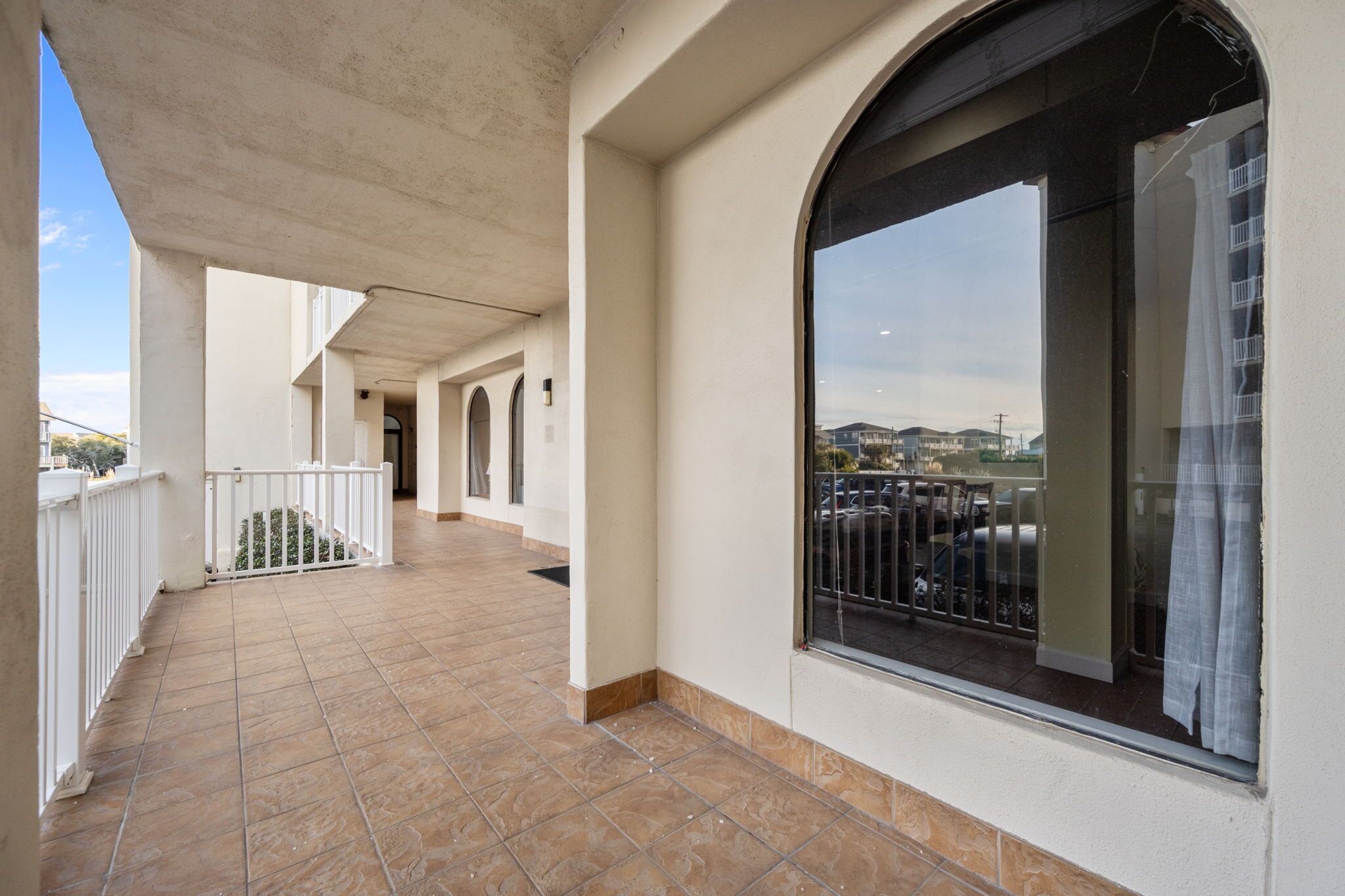 Un balcon fermé doté d’un sol carrelé, de balustrades blanches et d’une grande fenêtre offrant une vue sur le paysage urbain.