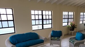 Ein Zimmer mit weißen Korbmöbeln, darunter Sofas und Sessel, die vor großen Fenstern mit Meerblick angeordnet sind.