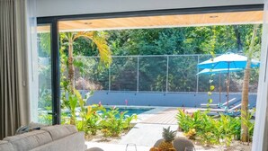 En matplats med ett bord för fyra personer, en soffa och utsikt över en pool och grönområden.