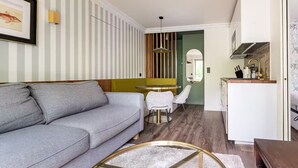 En moderne stue med en grå sofa, et rundt sofabord og et spiseområde med grøn væg og stribet tapet.