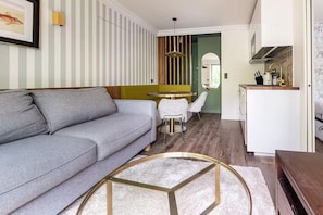 A modern living room with a grey sofa, a round coffee table, and a dining area with a green wall and striped wallpaper. - Apartment near Mouffetard (Paris)